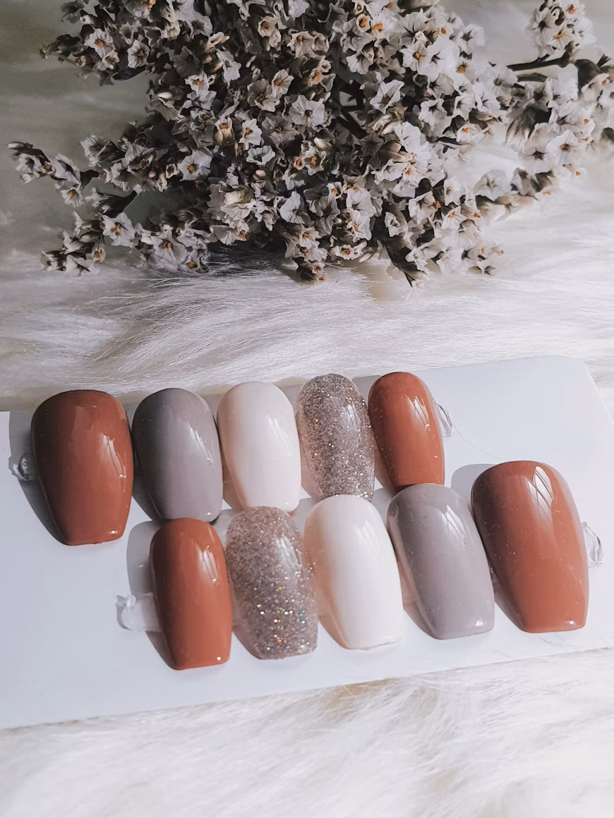 Ten neutral and glitter press-on nails arranged on a white display card.
